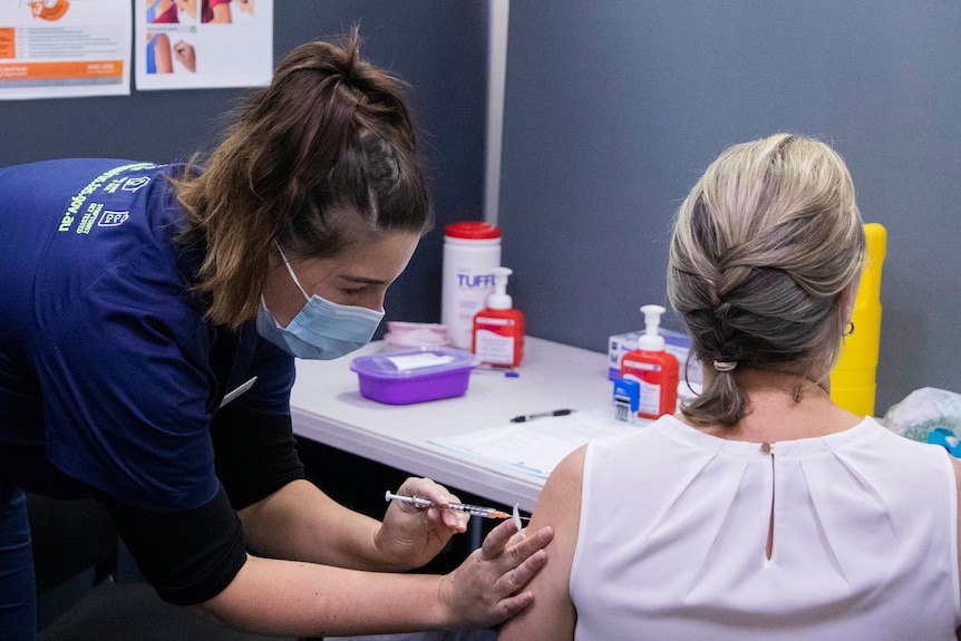 Nurse giving vaccine to female patient.