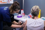 Nurse giving vaccine to female patient.