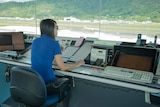 An air traffic controller sits at a desk with a full view of the runways and both terminals at Cairns Airport.
