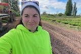 A woman in a high-vis top standing in a field with a tractor in the background