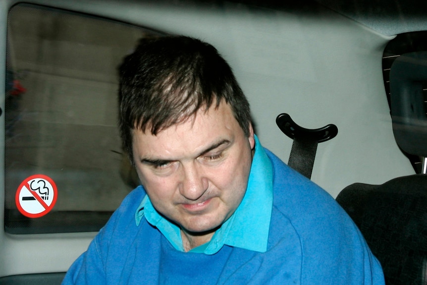 a man in a blue jumper looks down while sitting in the abck of a van 