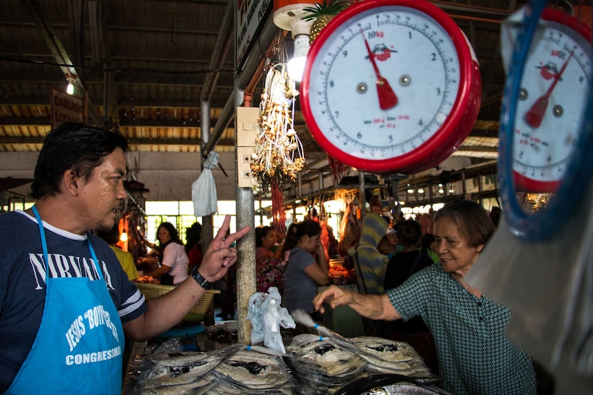 A fish vendor negotiates with a customer at a market in the Philippines.