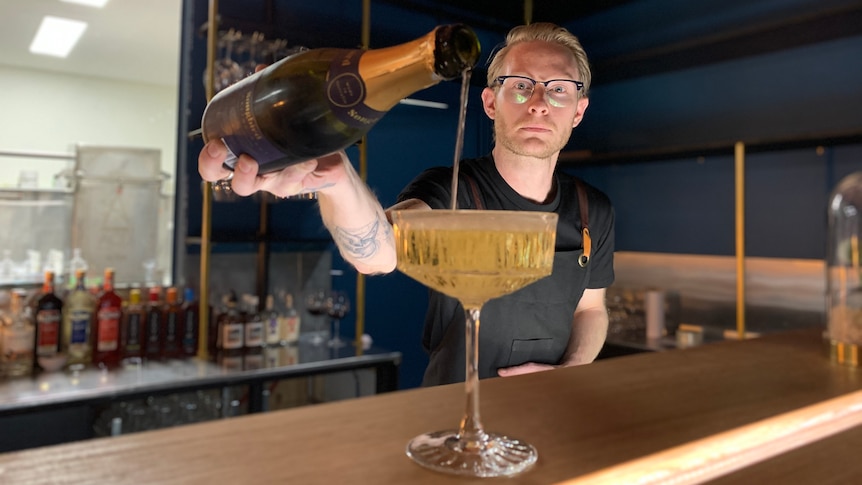 A bartender pours wine into a glass on a bar.