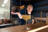 A bartender pours wine into a glass on a bar.