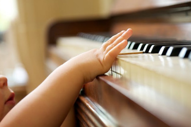 A child stretches up to play one note on a piano while standing.