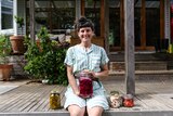 Meg Ulman at home sitting on her verandah holding a jar of fermented vegetables.