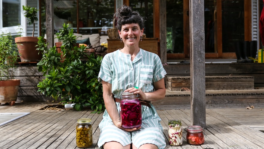 Meg Ulman at home sitting on her verandah holding a jar of fermented vegetables.