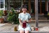 Meg Ulman at home sitting on her verandah holding a jar of fermented vegetables.