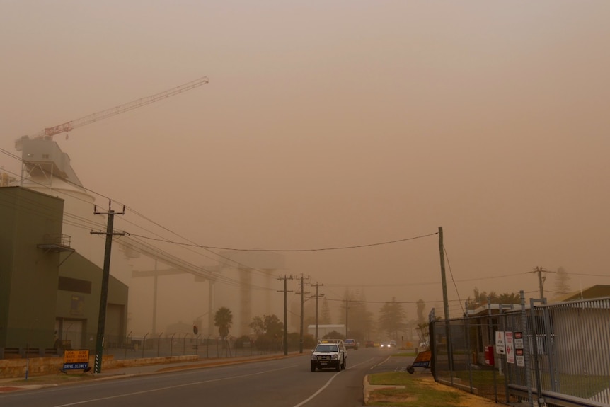 A ute drives down Marine Terrace in Geraldton, in front of silos obscured by dust.