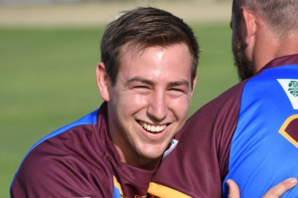 A smiling young man in a rugby league uniform hugs a teammate.