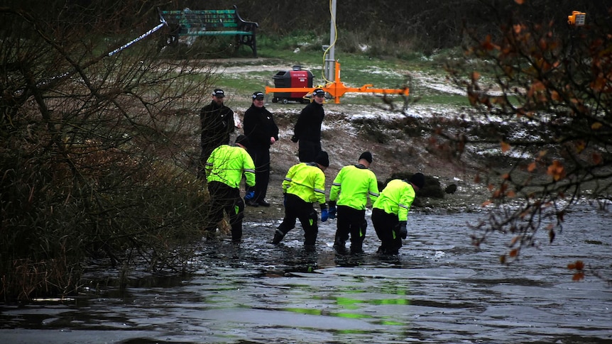 Four police officers in bright yellow hi-vis tops wade through water.