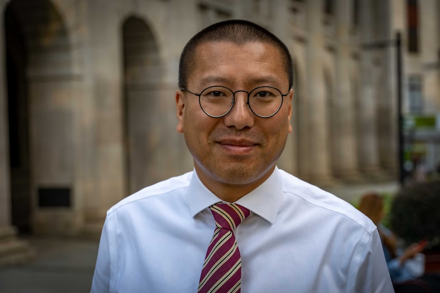 A portrait of a Hong Kong man in glasses and a suit.