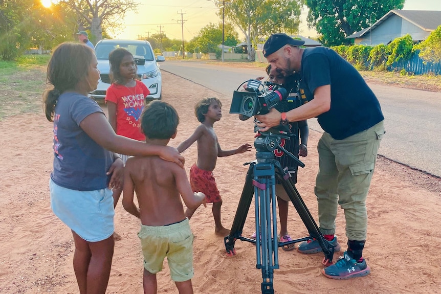Cameraman filming with camera on a tripod as Indigenous children watch on.