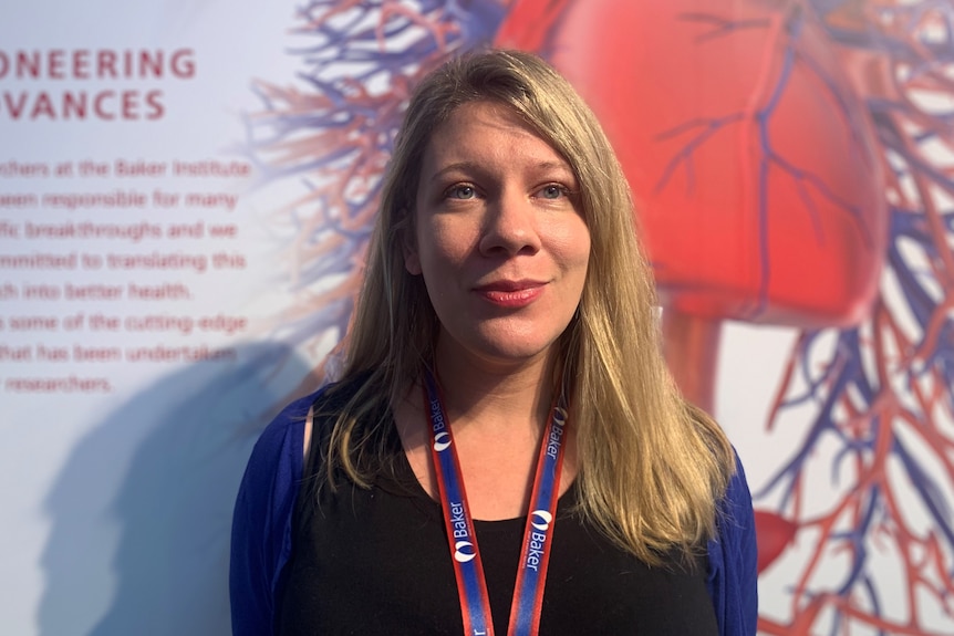 Liz Paratz standing in front of a large graphic of a heart with information about research.