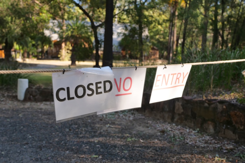 Signs hanging on a rope that reads, closed no entry. Trees behind.