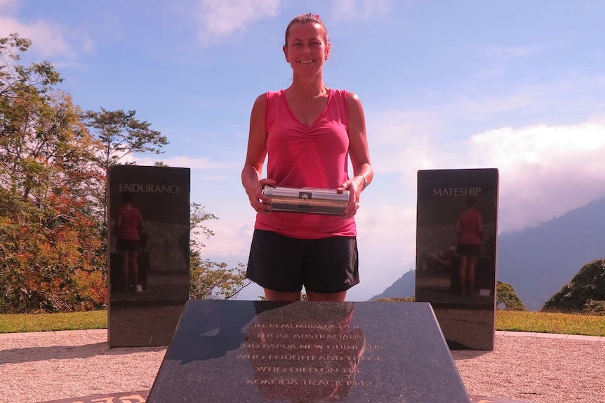 Anita Jakins standing in front of the Kokoda Memorial in the Isorera Valley, holding the Roll of Honour