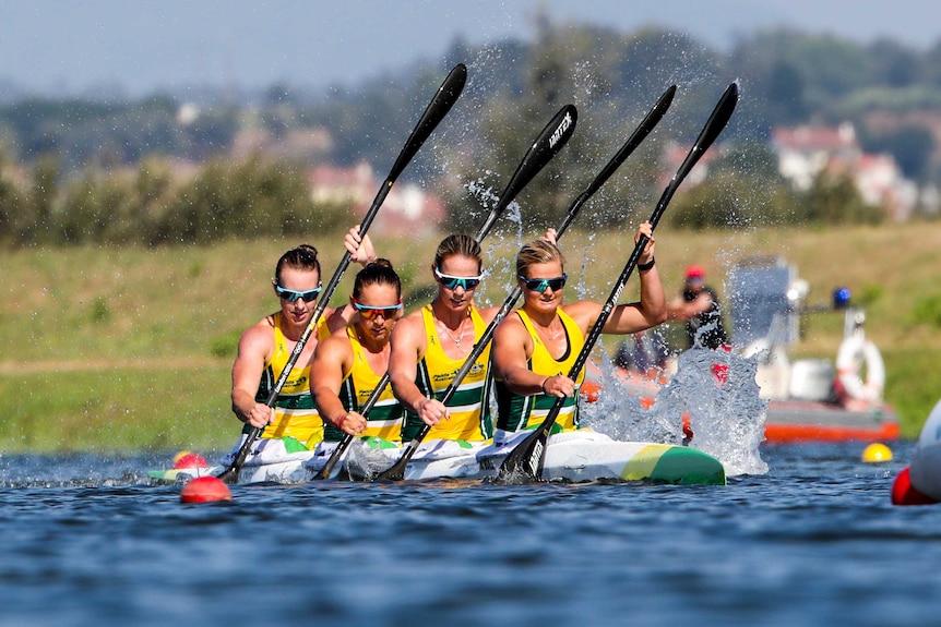 A team of four Australian kayakers race, with their blades cutting through the water.
