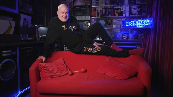 Man in a rage top and pants sitting on top of a red couch in the studio