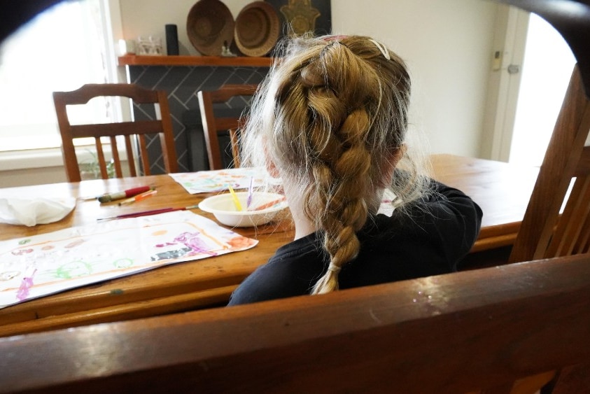 A young girl paints at a large kitchen table.