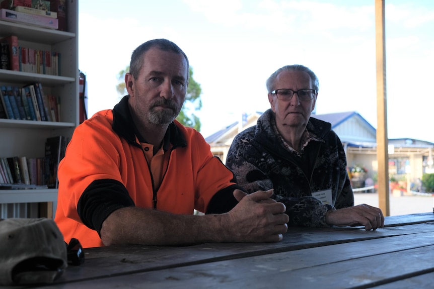 An elderly gentleman and his middle-aged son sit on a park bench at a caravan park. 