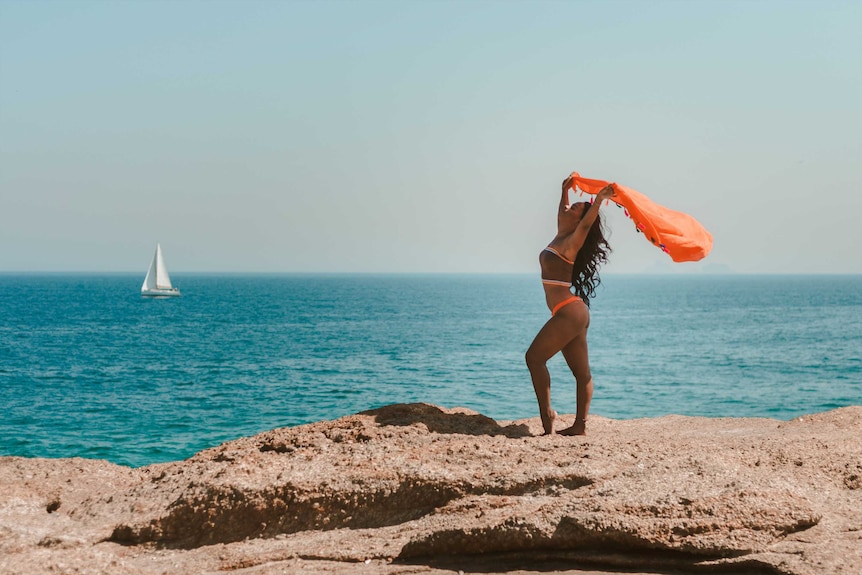 Woman standing in a bikini by the sea in a body confident power pose to depict how to make swimwear shopping less stressful.