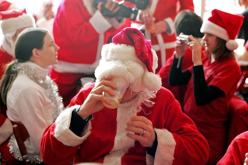 A man wearing a Santa outfit drinks a beer.