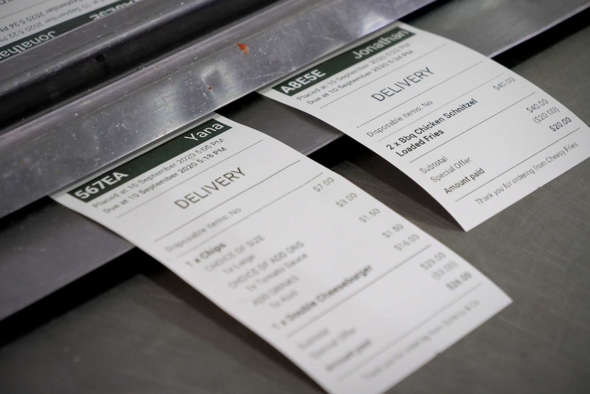 Food order receipts lie on a stainless steel bench