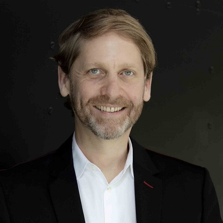 A close up man with light features smiling in a suit