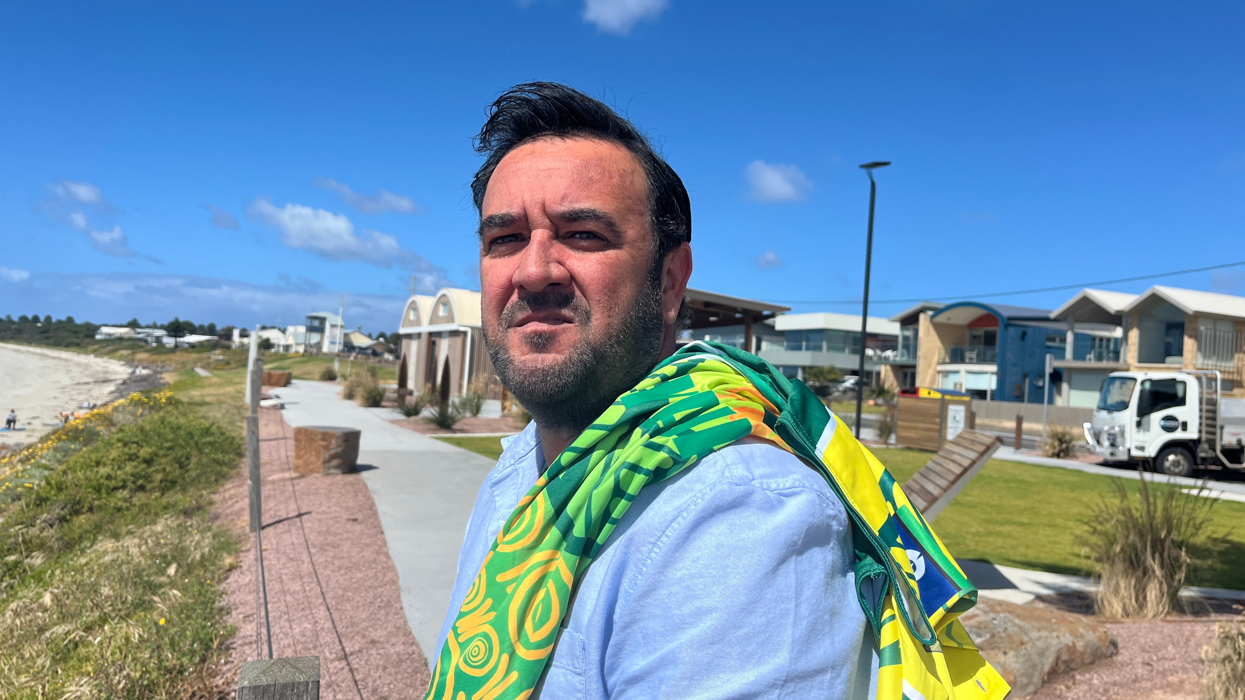Um homem está parado em frente a uma praia com uma camisa de críquete pendurada no ombro.