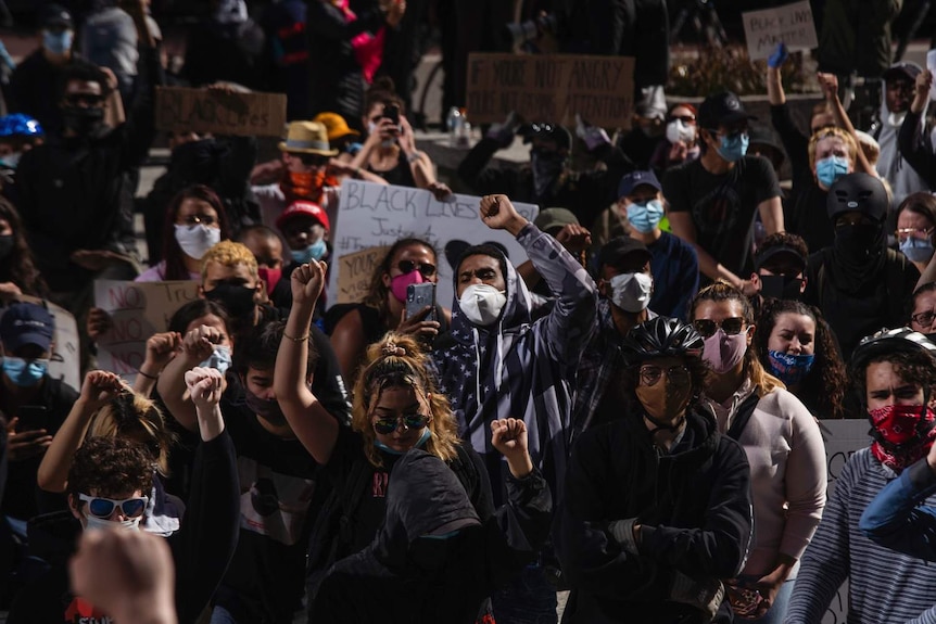 A large group of people gather in the night to protest while holding signs and raising fists.