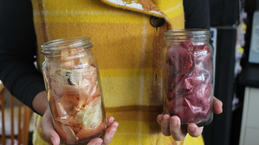 A person holds two jars in their hands, one full of red onion skins and the other full of white onion skins.