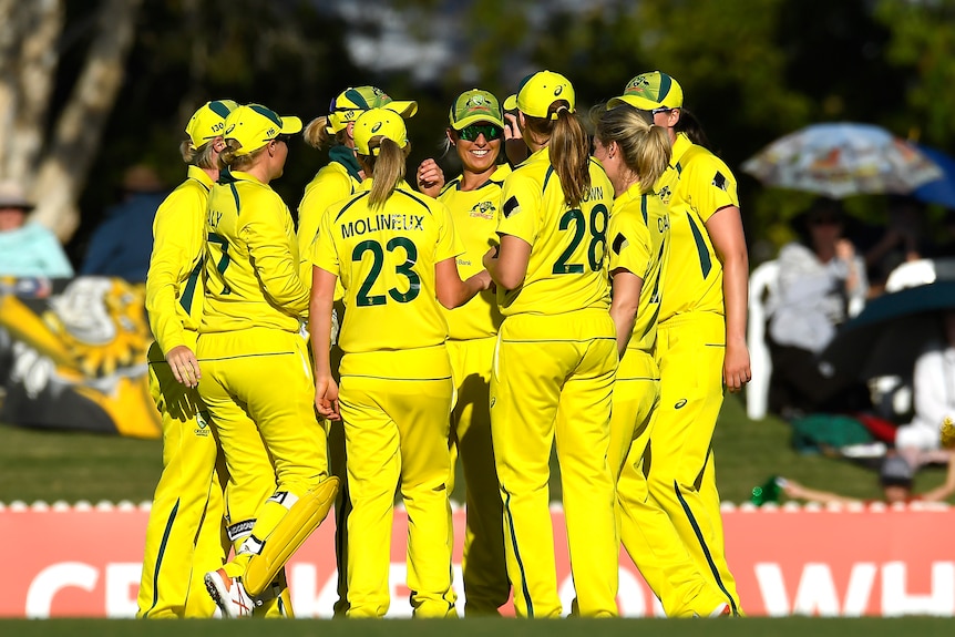 Australian team come together in a group, wearing yellow cricket kit