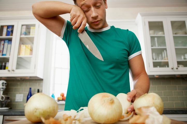 A man wipes away a tear while chopping onions.