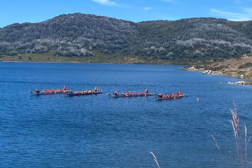 Four dragon boat row boats float in the Rockey Valley Lake at Falls Creek.