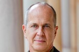 A profile photo of Peter Greste wearing a blue coat and green shirt.