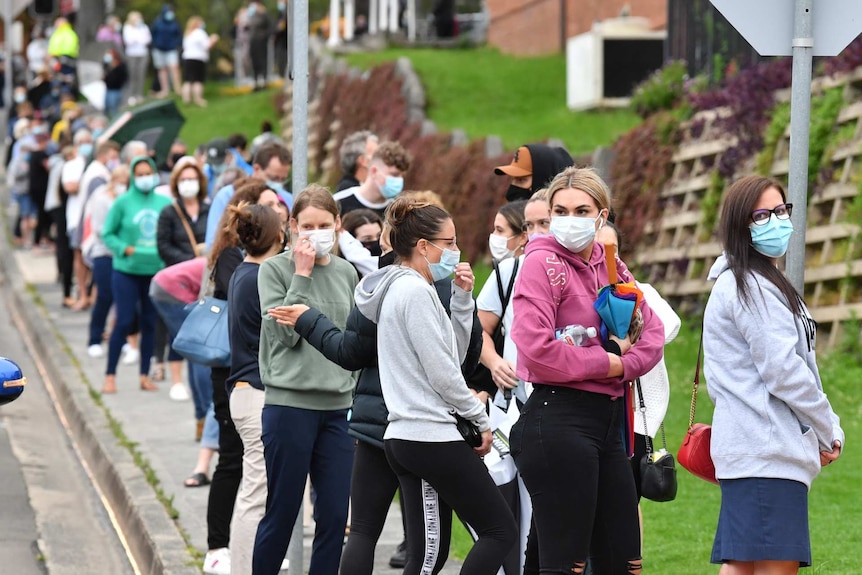 long queue of people waiting outside a hospital wearing masks