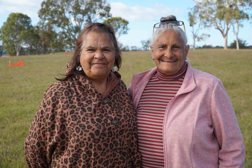 Two Aboriginal Elders look into the camera standing in an open paddock. 