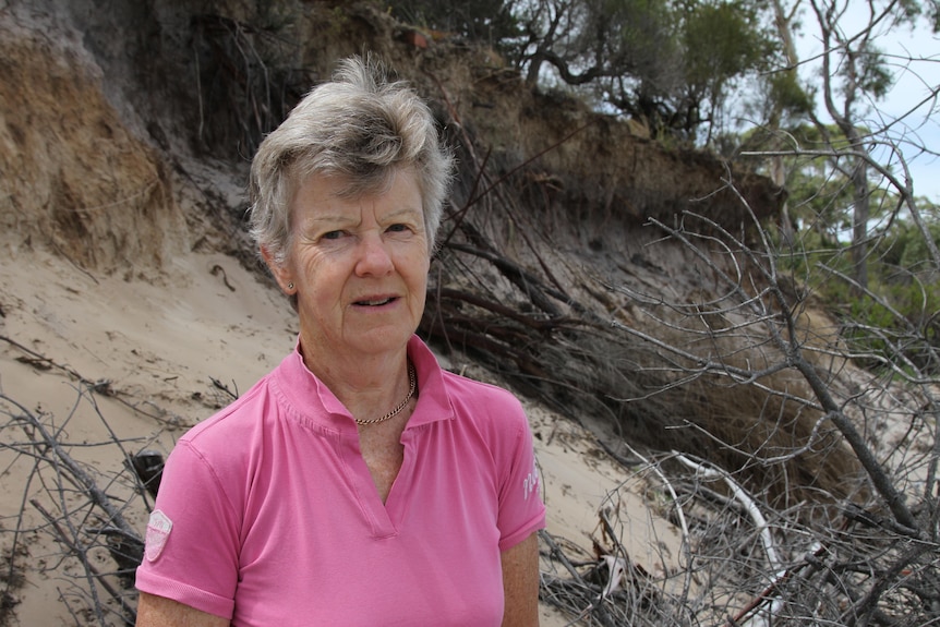 a woman in a pink shirt is standing on a beach in front of cliff where land has collapsed onto the beach