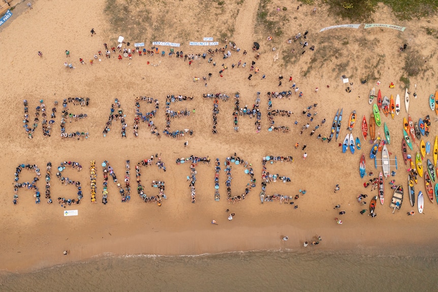 A drone shot of people creating a human sign on the beach that says WE ARE THE RISING TIDE.