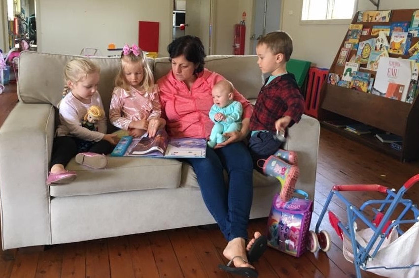 A mum reads a book to kids on a couch at Hamilton Community South Playgroup near Newcastle.
