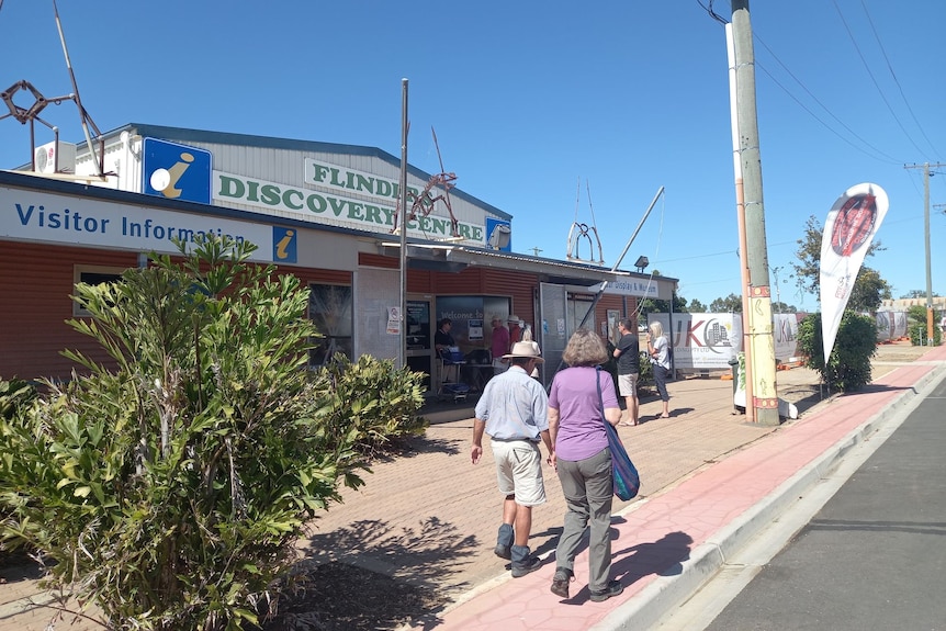 People lining up in the sun outside a metal building.