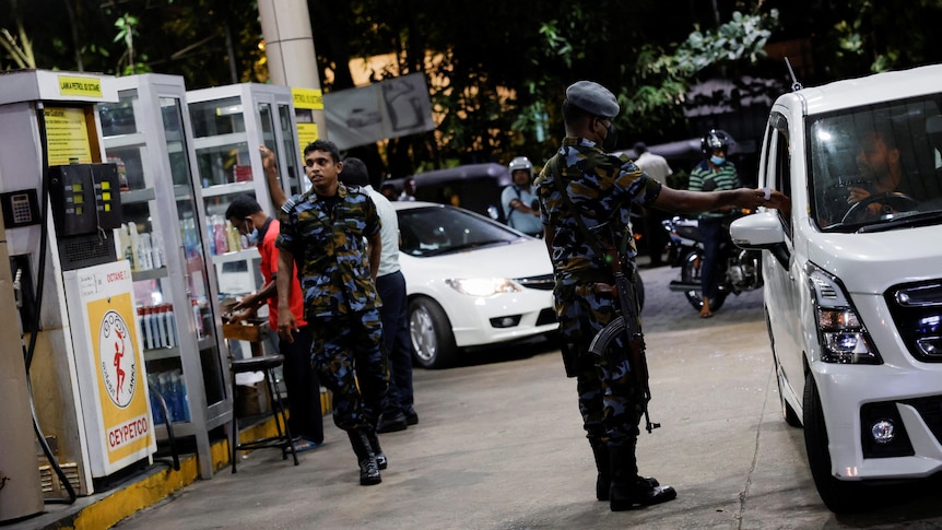 Picture of a man walking through a fuel station an armed man in security uniform checking cars