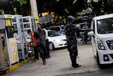 Picture of a man walking through a fuel station an armed man in security uniform checking cars