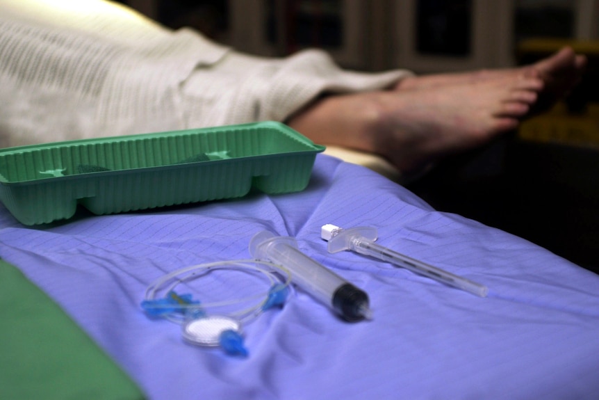 Una jeringa y algunos tubos médicos en una sábana azul frente a un paciente