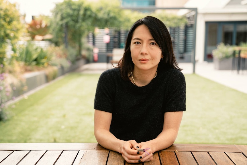 A woman with black hair sits at a table