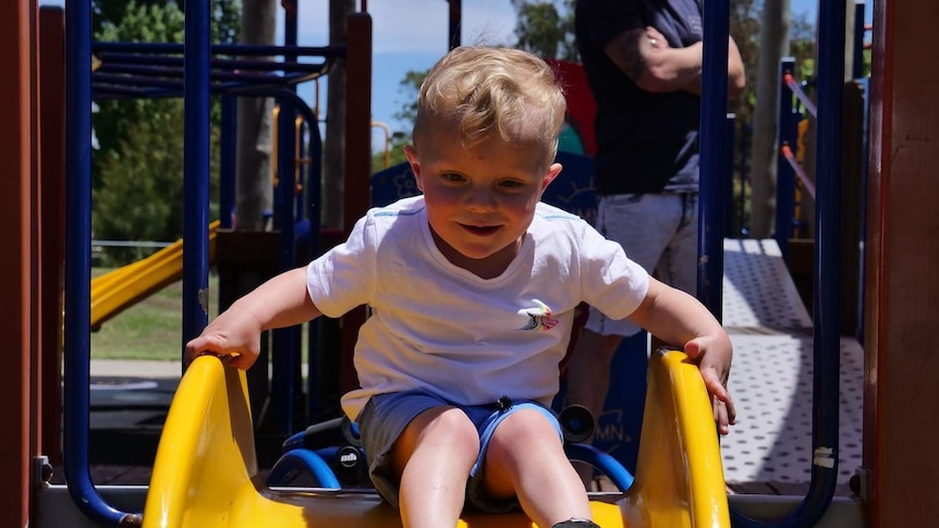 A little boy smiles at the top of a yellow slide