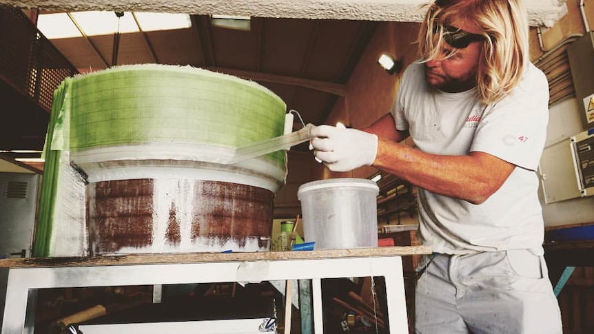 Andrew Turton works on a prototype Seabin in a workshop, peeling off tape from the round structure.