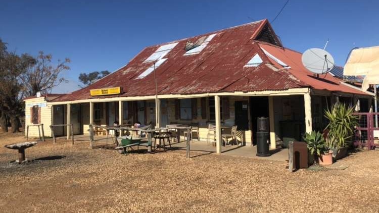 The outside of a rural hotel, with the remains of a campfire in the foreground.