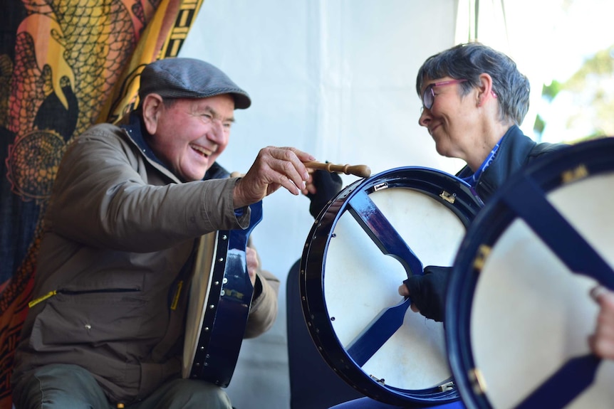 Festival goers laughing while playing a traditional Irish drum.