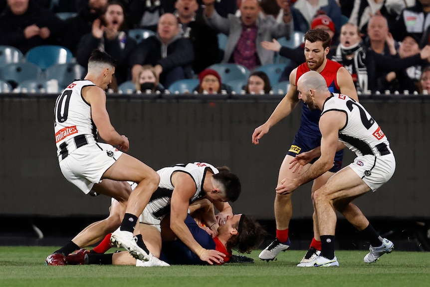 Collingwood players watch on as a Magpies player lies on top of a Demons player after driving him into the ground.